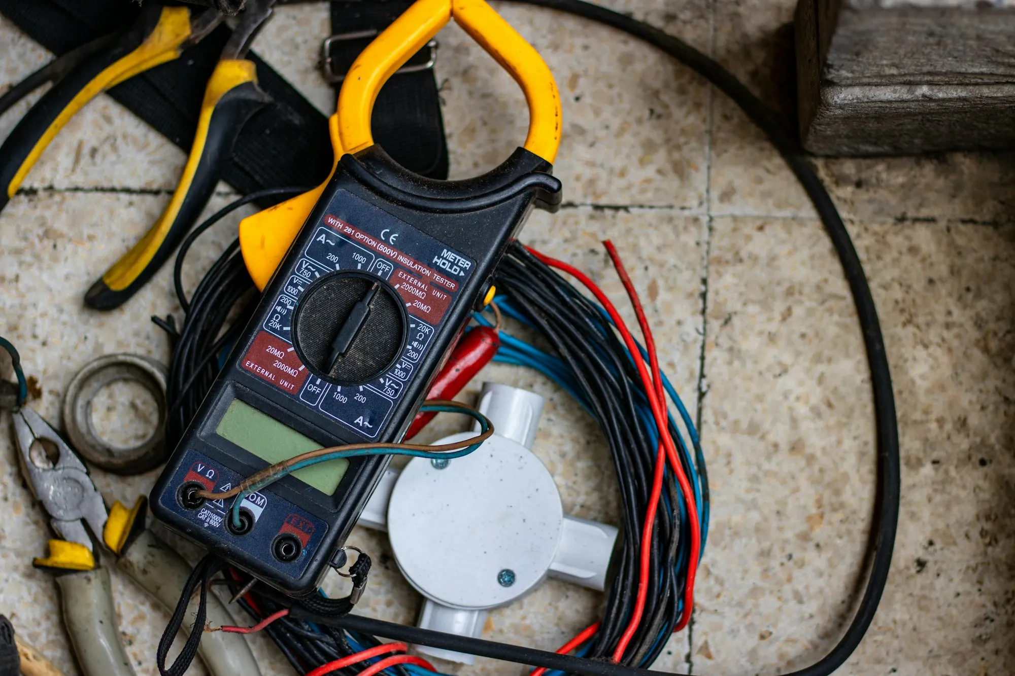 Clamp meter, pliers and colored wire spread out on a tiled floor